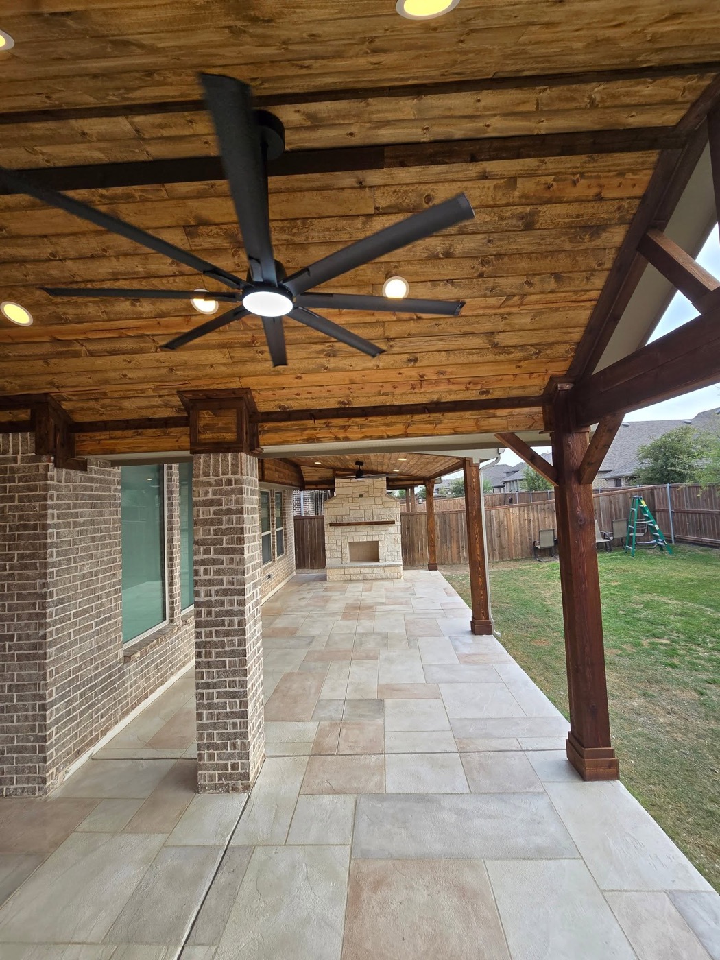 Long covered patio with oversized ceiling fan and outdoor fireplace