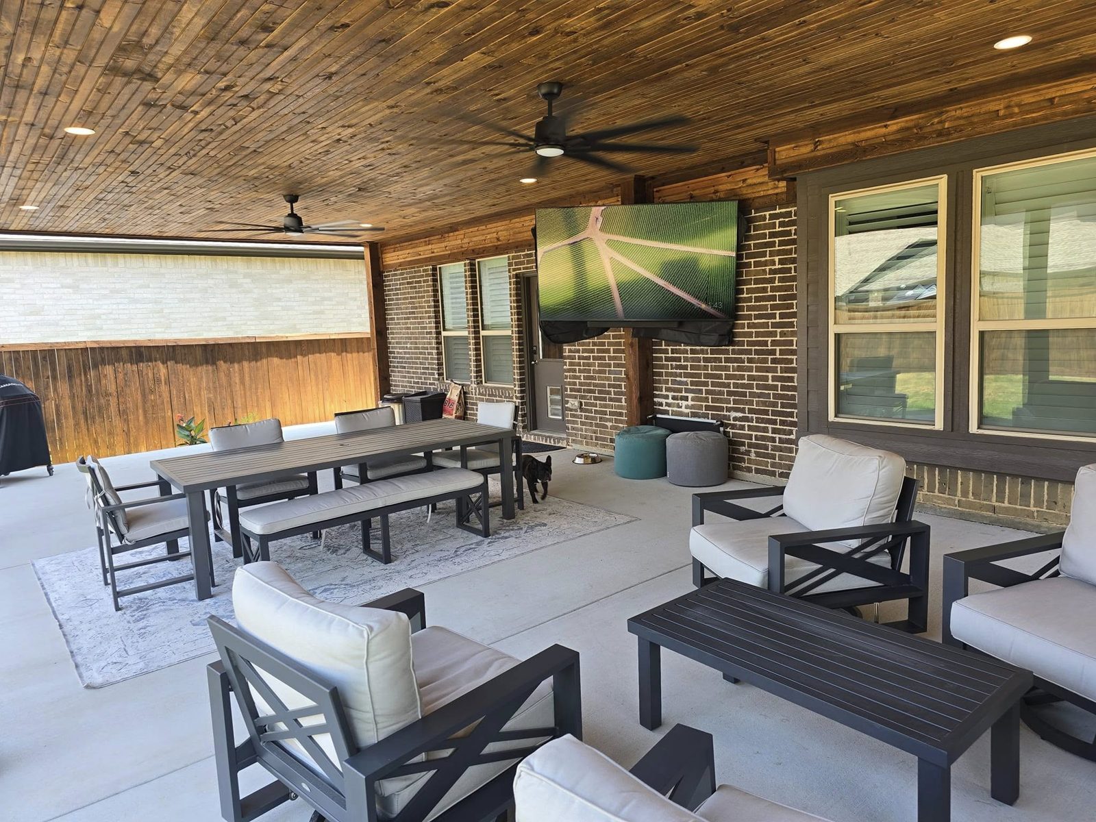 Under a covered patio with stained wood ceiling, fans, and a mounted TV