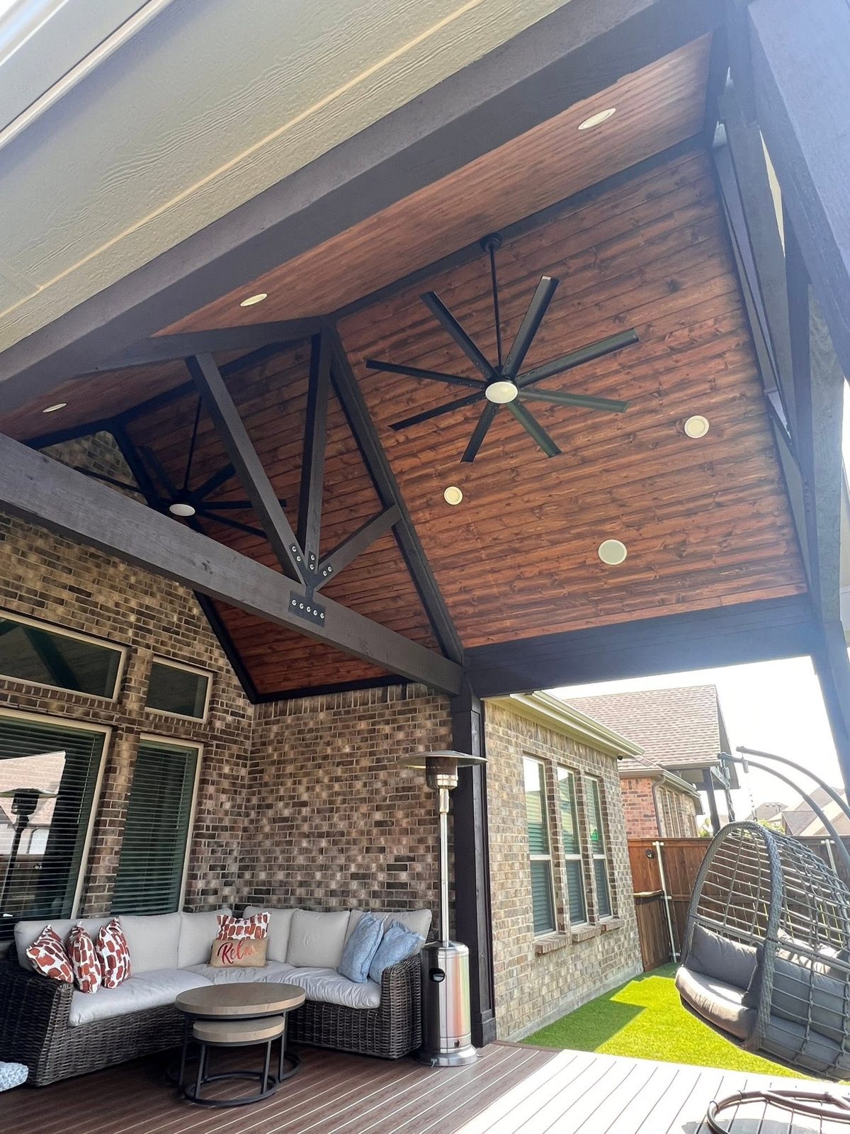 Vaulted stained wood ceiling with exposed trusses and a large fan over a covered patio