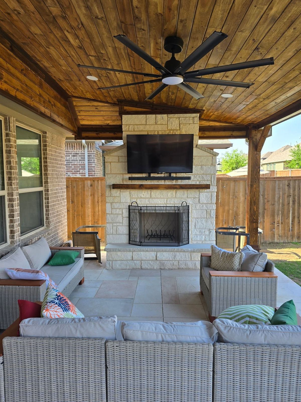 Covered outdoor room with a stone fireplace, stained wood ceiling, and lounge seating