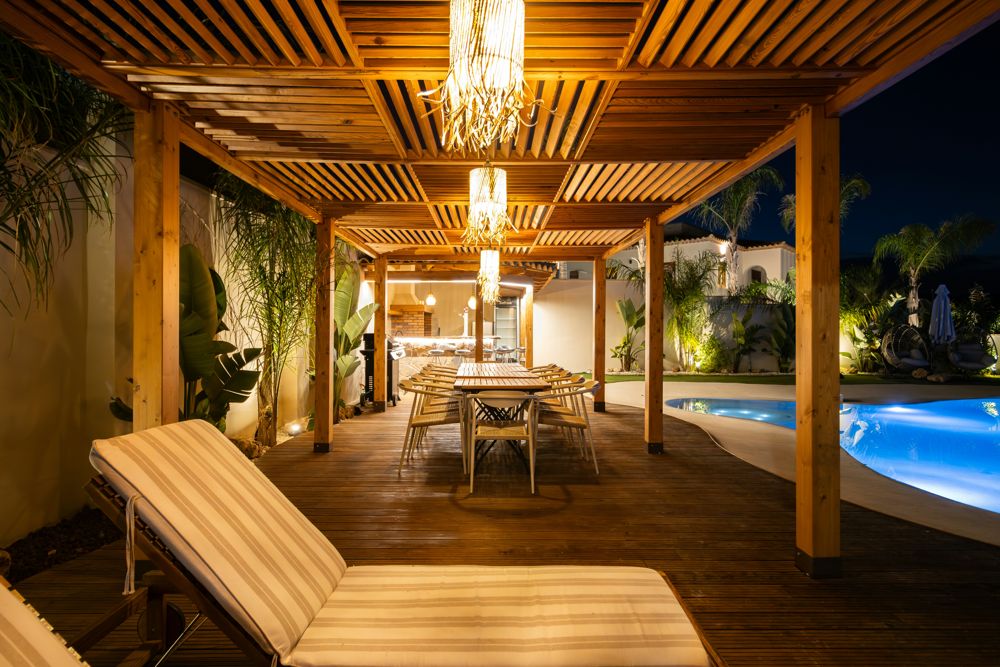 Covered patio with slatted pergola lit at night