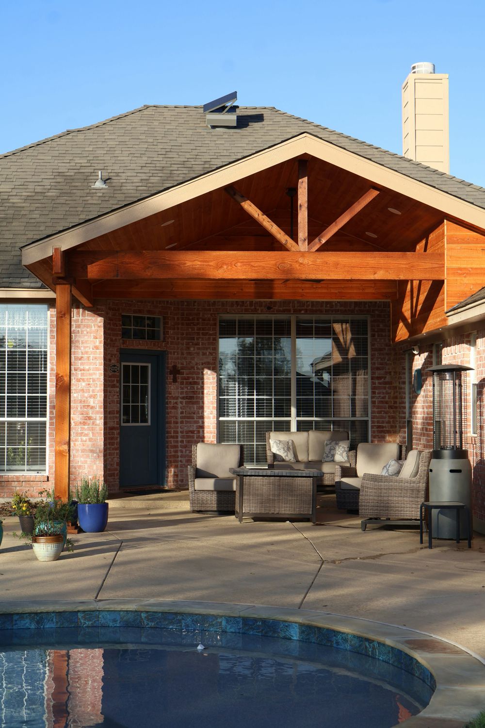 Gabled patio cover attached to a brick home by a pool