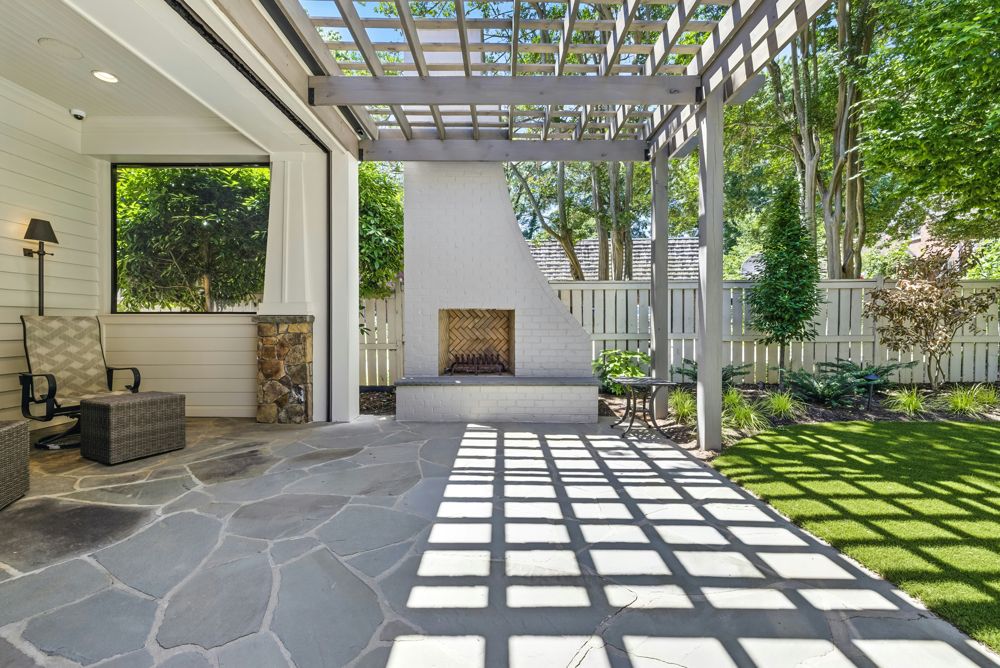 White pergola over a flagstone patio with a fireplace